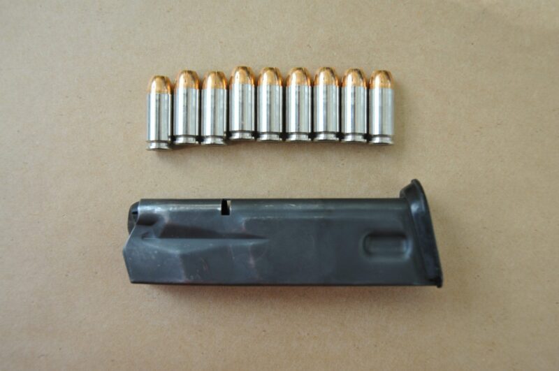 A SIG Sauer pistol magazine lays on a piece of brown paper. Nine bullets are arranged in a row above it.