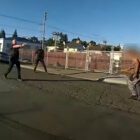 A shirtless man holding a handsaw blade approaches two deputies, one of whom is pointing a handgun, outdoors during daytime, from the perspective of the body camera of a third deputy, who is pointing a Taser at the man.