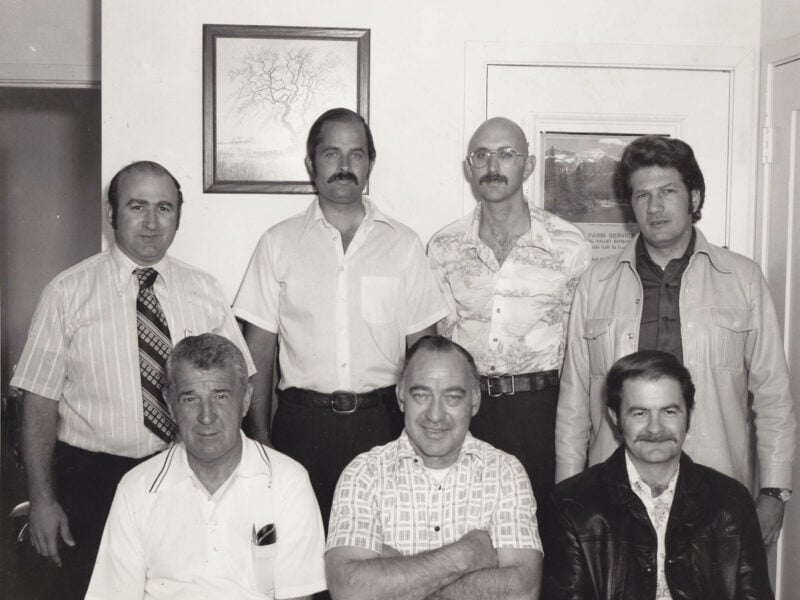 Five Vallejo police officers pose indoors with another man in a black and white group photograph taken in the 1970s or early 1980s. Front row, left to right: John Lynch, Peter Zander, Ronald Guerra. Back row: unknown, Herbert Shrum, Burky Worel, Louis Baldino.