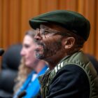 Then-Vallejo Councilmember Hakeem Brown speaks at a city council meeting on police reform on Dec. 6, 2022. Brown is a Black man in his mid-40s wearing glasses, a green Pendleton-style cap and green vest over a black shirt. He has a goatee.