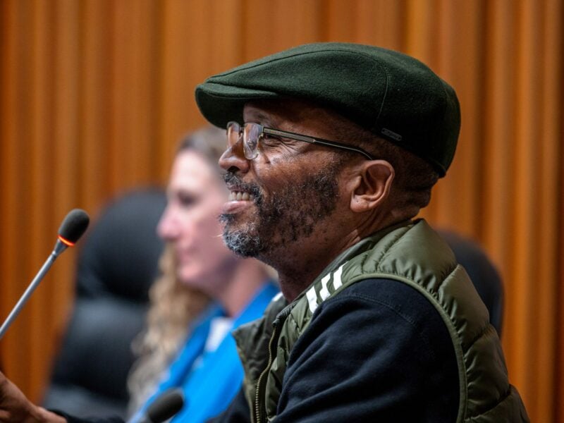 Then-Vallejo Councilmember Hakeem Brown speaks at a city council meeting on police reform on Dec. 6, 2022. Brown is a Black man in his mid-40s wearing glasses, a green Pendleton-style cap and green vest over a black shirt. He has a goatee.