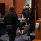 A young Black man is wheeled into a courtroom while surrounded by Solano County Sheriff's deputies.