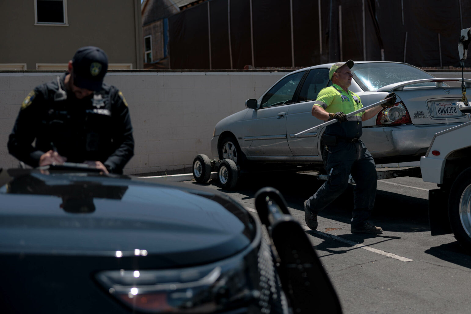 A Vallejo police officer fills out paperwork while a tow truck driver prepares to tow a silver sedan.