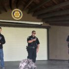 Three police personnel speak to an audience in a small, covered outdoor amphitheater.