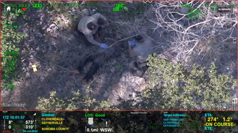 An overhead image, taken from a sheriff's office helicopter, of two deputies rendering aid to a dying man in heavy, dry brush.