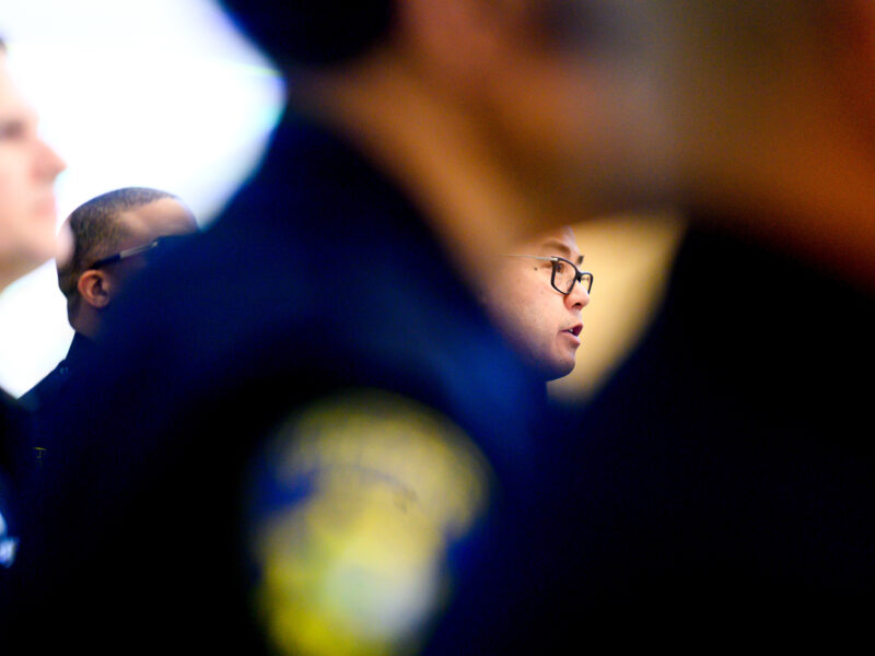 A bespectacled police chief is seen framed by officers, who are out of focus.