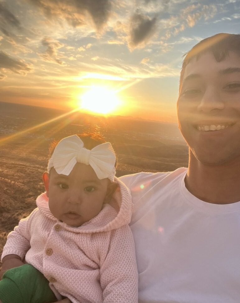 A young man holding a baby at susnet