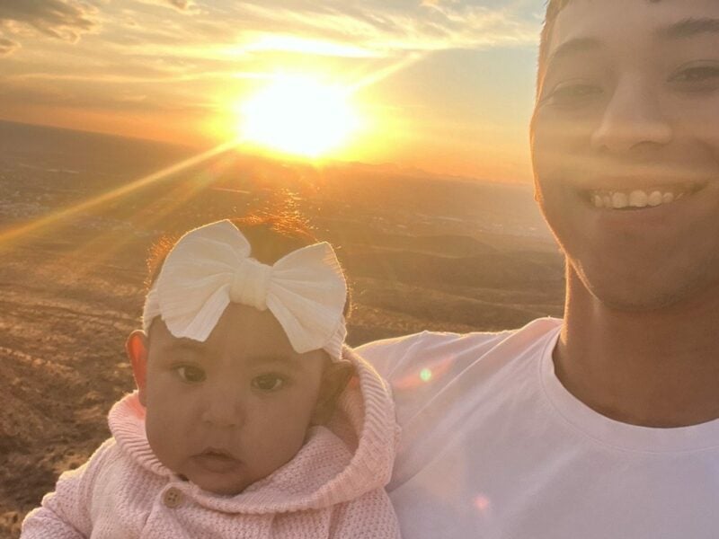 A young man holding a baby at sunset
