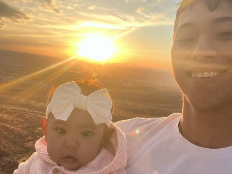 A young man holding a baby at sunset