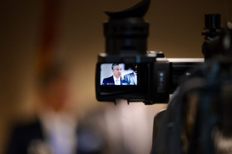 Attorney General Rob Bonta as seen in a television camera monitor during an indoor press conference.