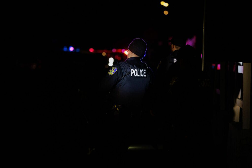 Several Vallejo police officers are lit by police lights at night.