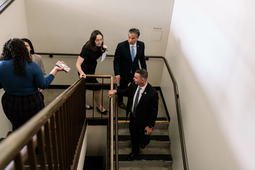 California Attorney General Rob Bonta and his entourage walk down a staircase as seen from above.