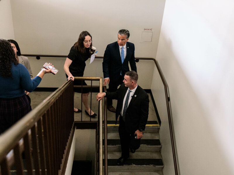 California Attorney General Rob Bonta and his entourage walk down a staircase as seen from above.