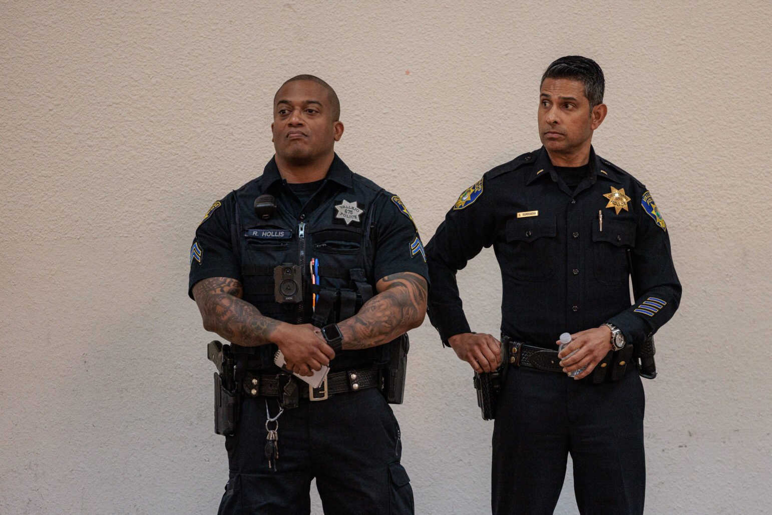 Two Vallejo police officers stand against a wall during a department town hall.