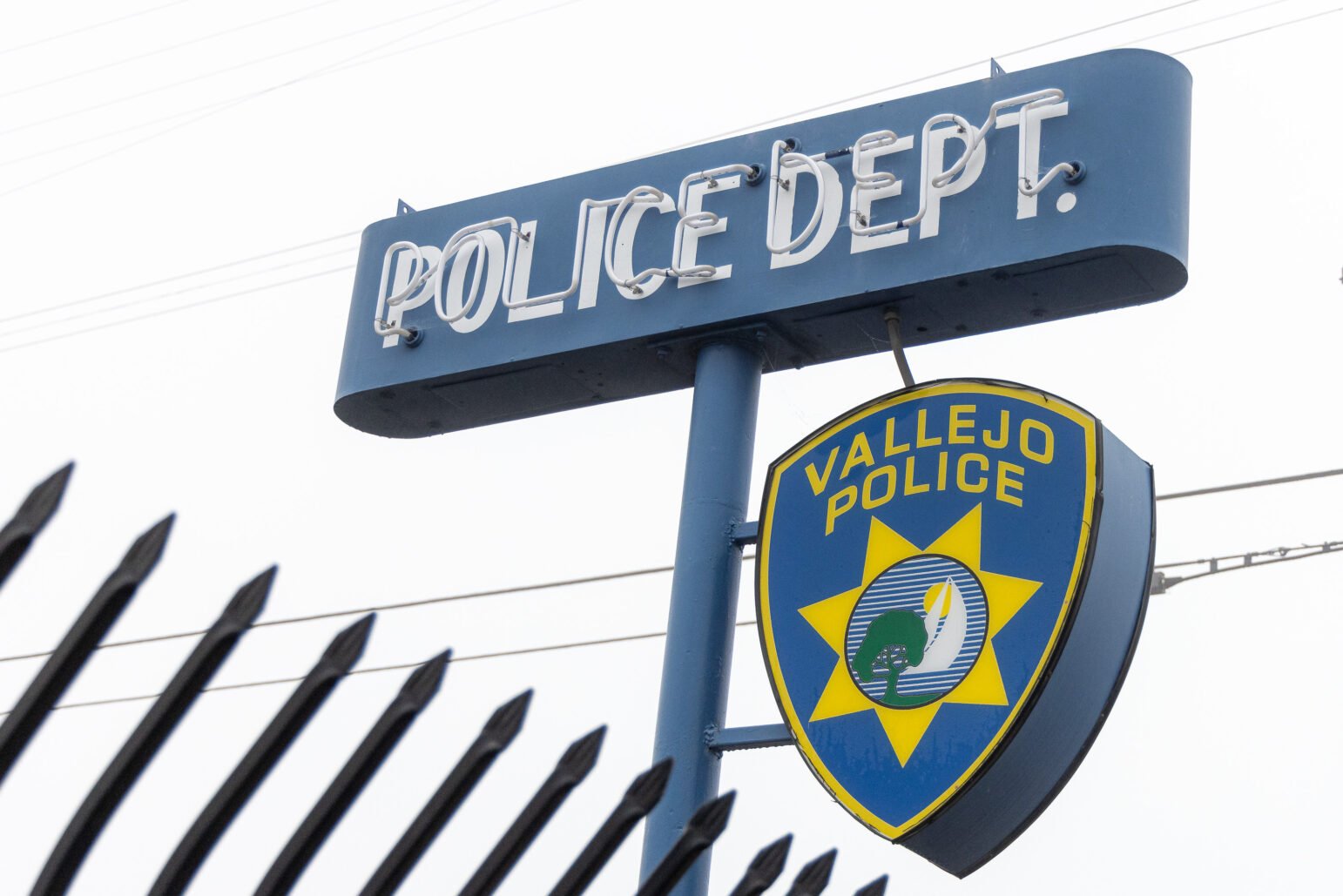 The neon Vallejo Police Department sign, with a lighted pendant reading, "Vallejo Police" below it, framed by sharpened, curved iron bars.