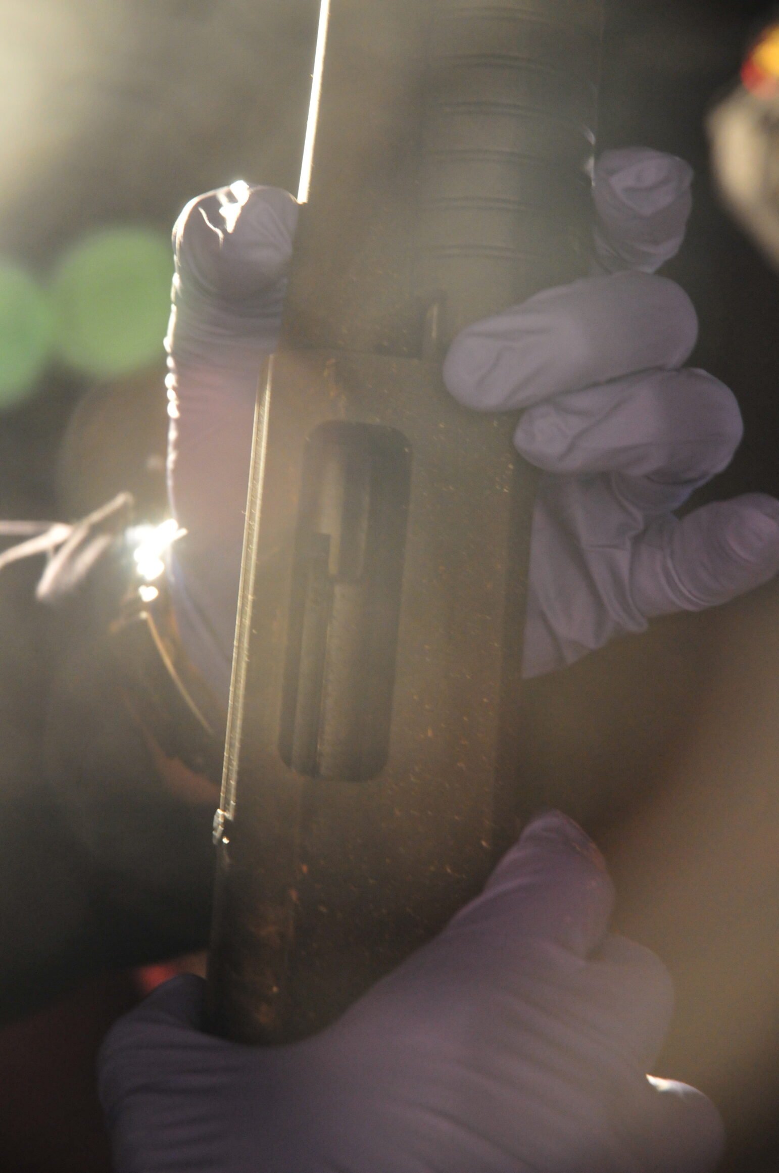 A close-up shot of a person's purple nitrile-gloved hands holding a shotgun vertically as light spills around the edges of the image.