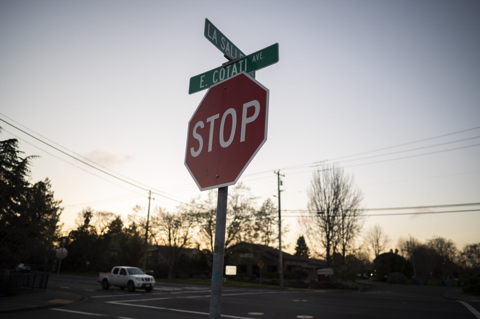 Dusk scene featuring a stop sign at the intersection of Lasalle Ave. and E. Cotati Ave. The sign is in sharp focus with a soft-focus background, including a vehicle passing by and the fading light of the sky.
