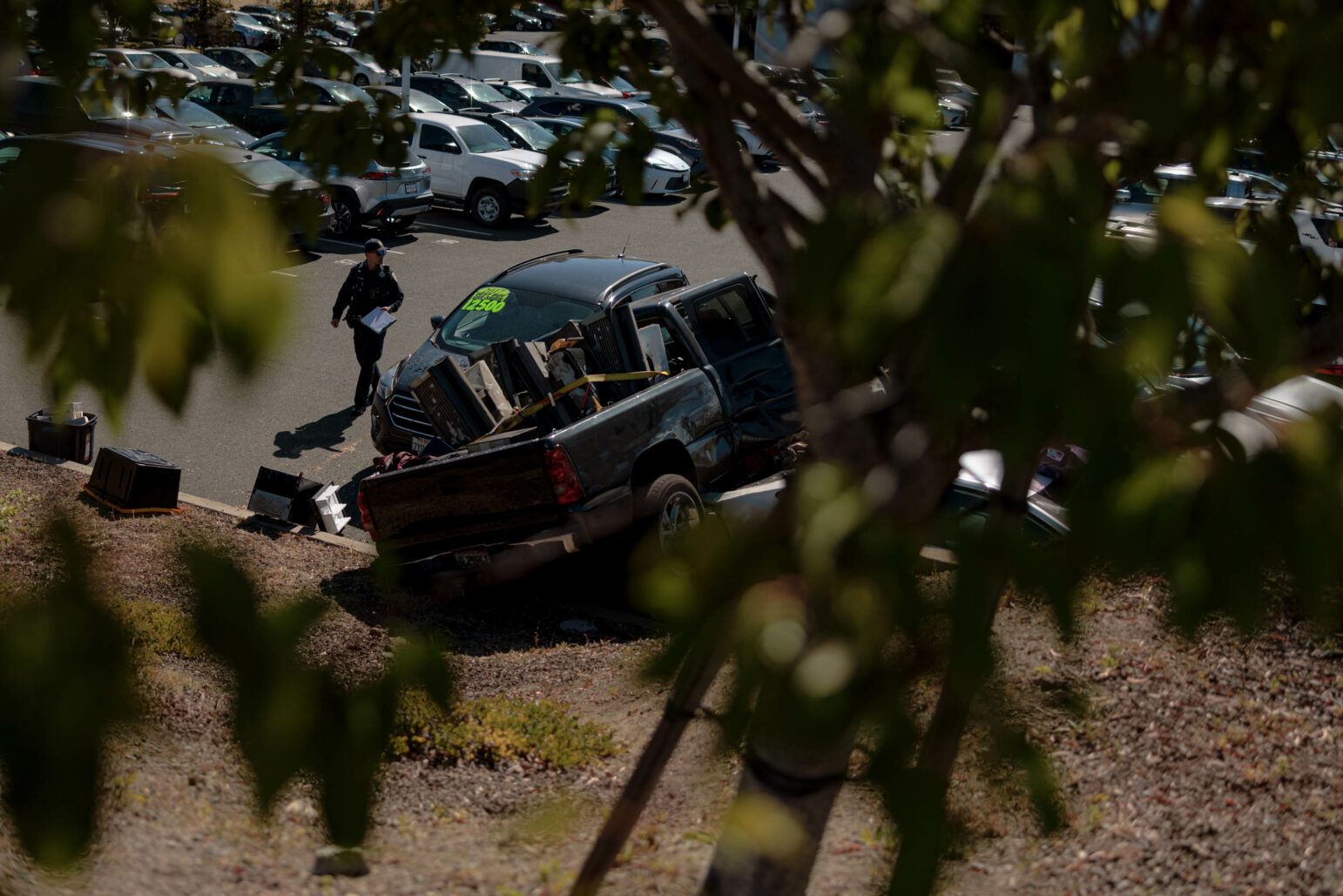 A Vallejo police officer walks around a truck that crashed into several other vehicles outside during daytime.