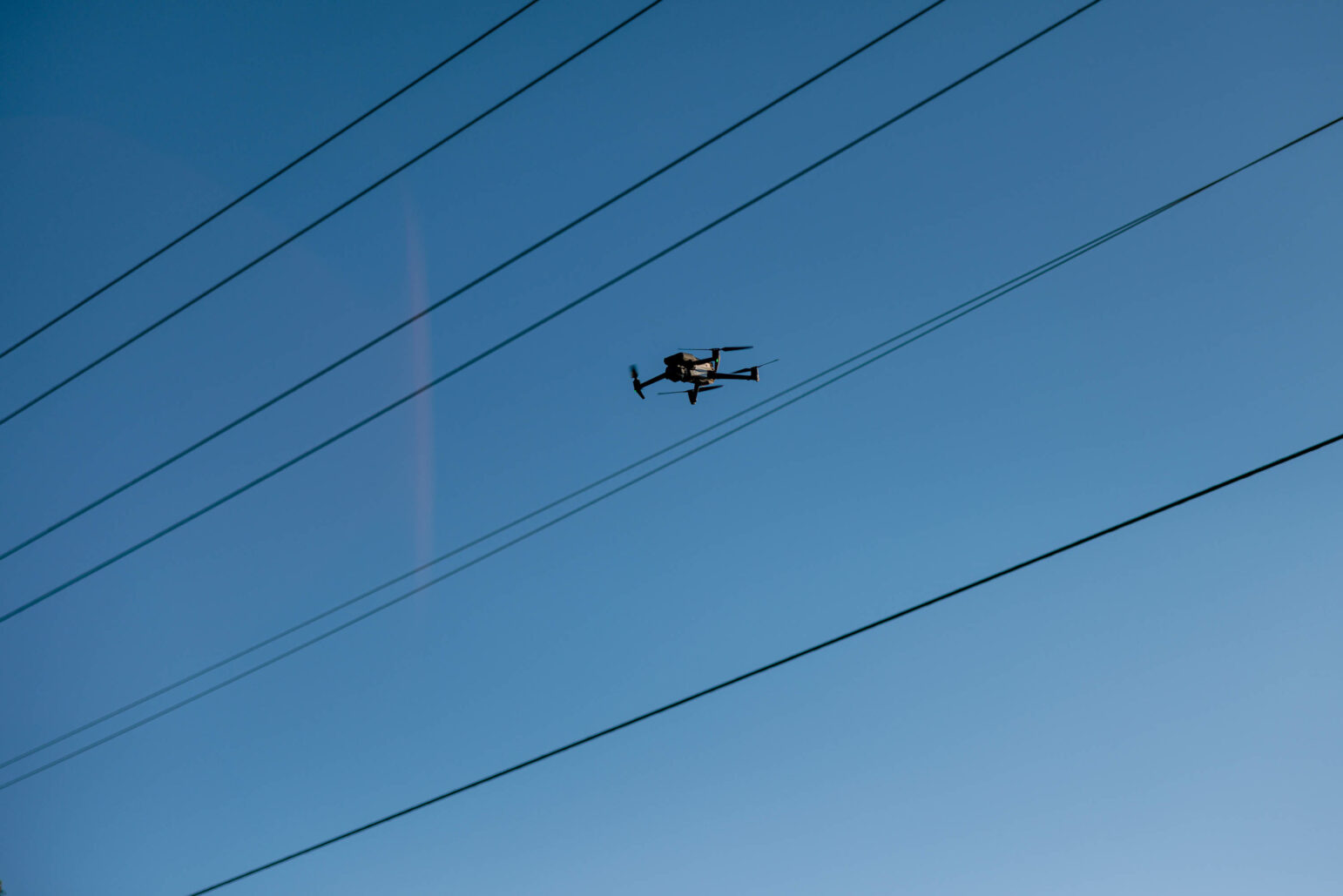 A police drone is flying in the sky above power lines.