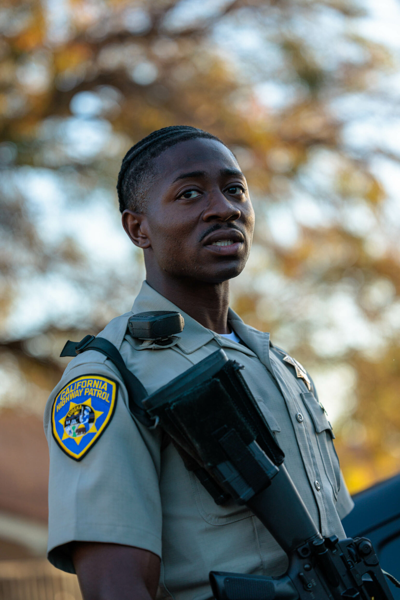 A close-up portrait of a California Highway Patrol officer in uniform. The officer is looking ahead with a serious expression, and the background is slightly blurred.