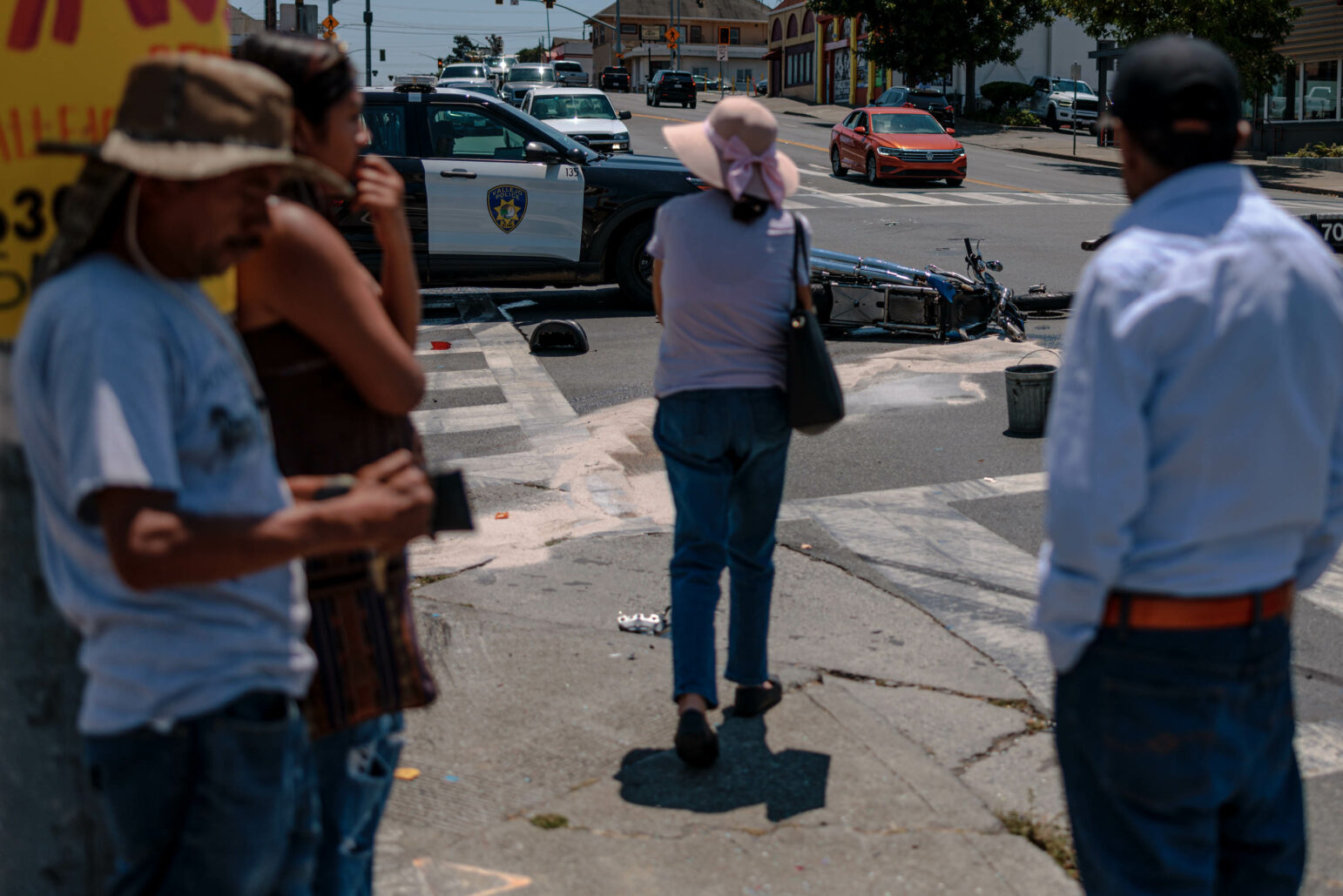 People gather around a crashed motorcycle with Vallejo police SUVs in the background.