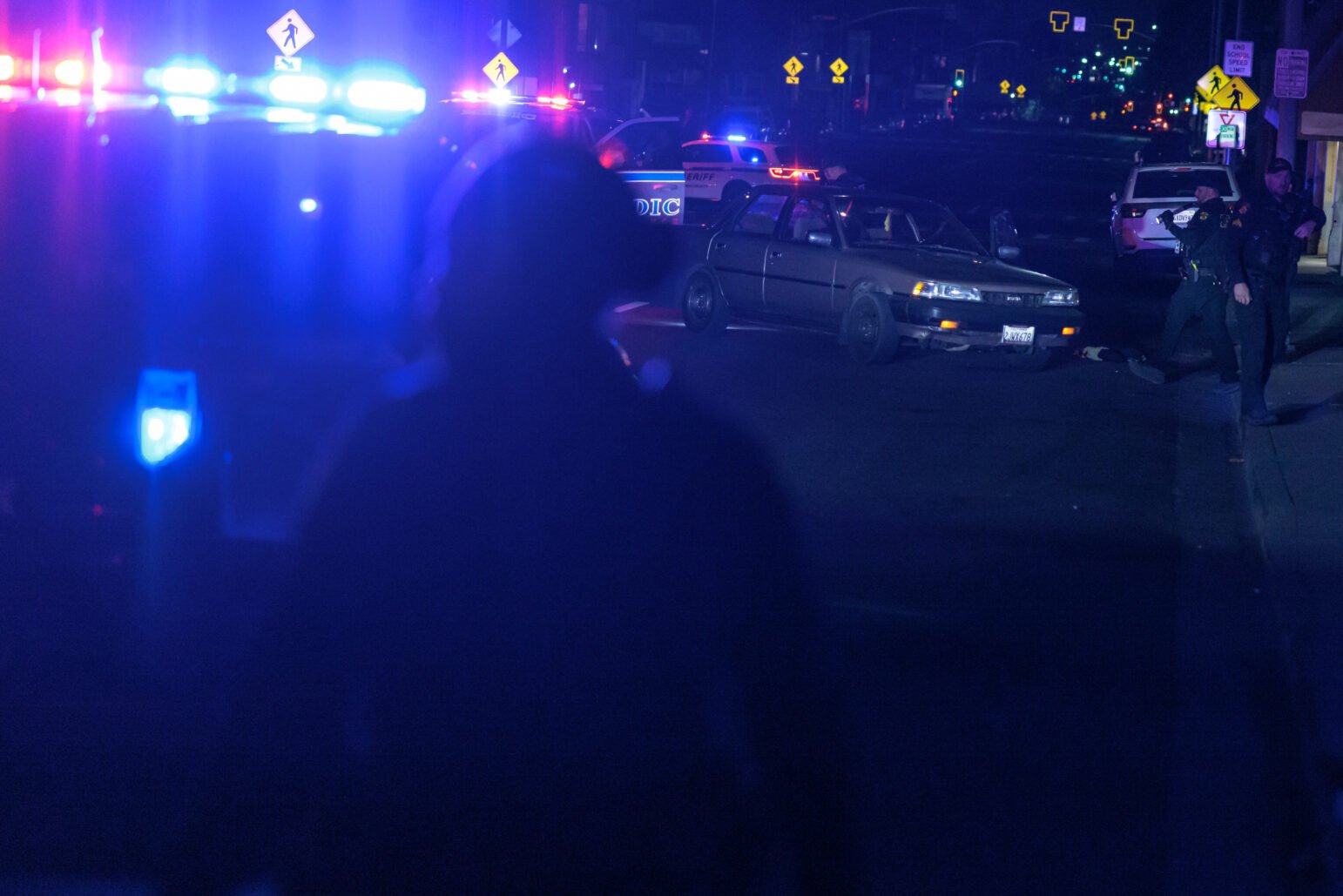 A sedan sits unoccupied among flash police lights as Vallejo police and Solano County Sheriff's deputies search for evidence of a shooting at night.