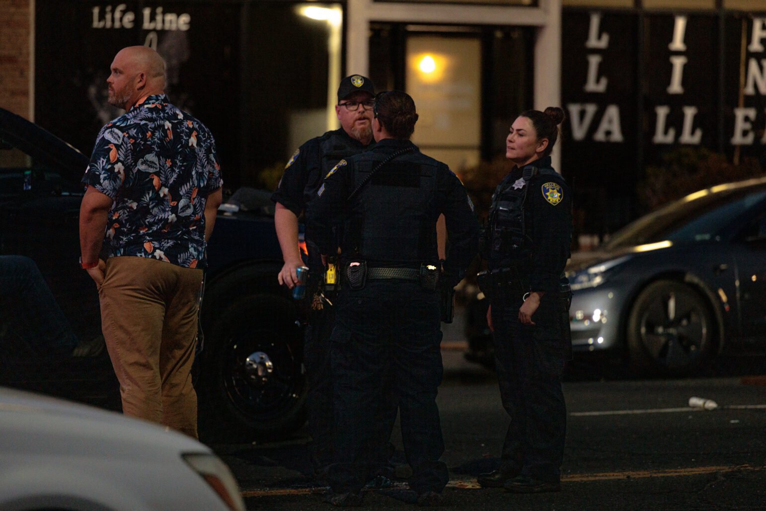 A group of individuals Vallejo police officers stand together on a dimly lit street. The officers, in dark uniforms, appear to be discussing something as they stand near a vehicle.