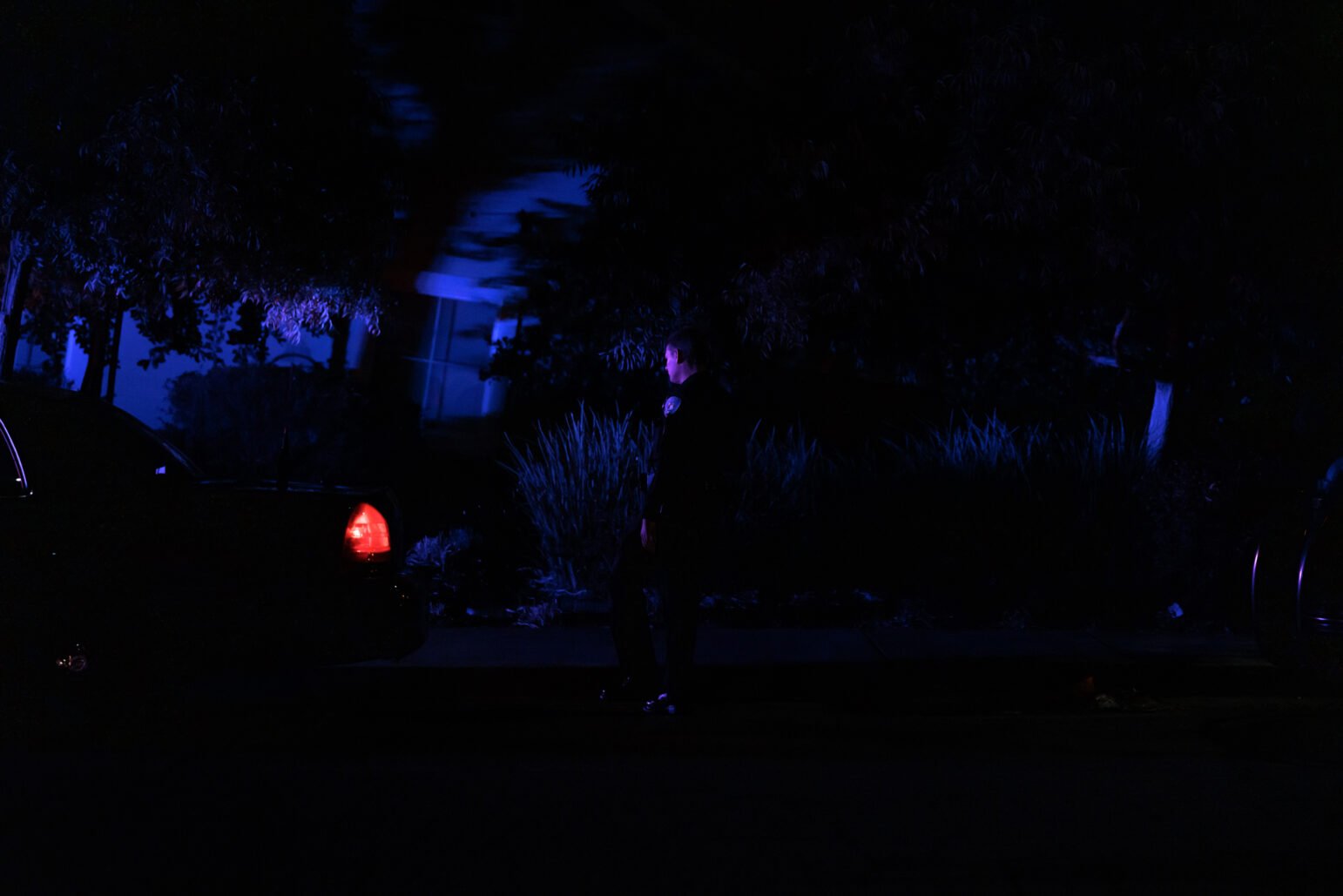 A Vallejo police officer arrives at the scene of a shooting at night. He is bathed in blue chiaroscuro light.