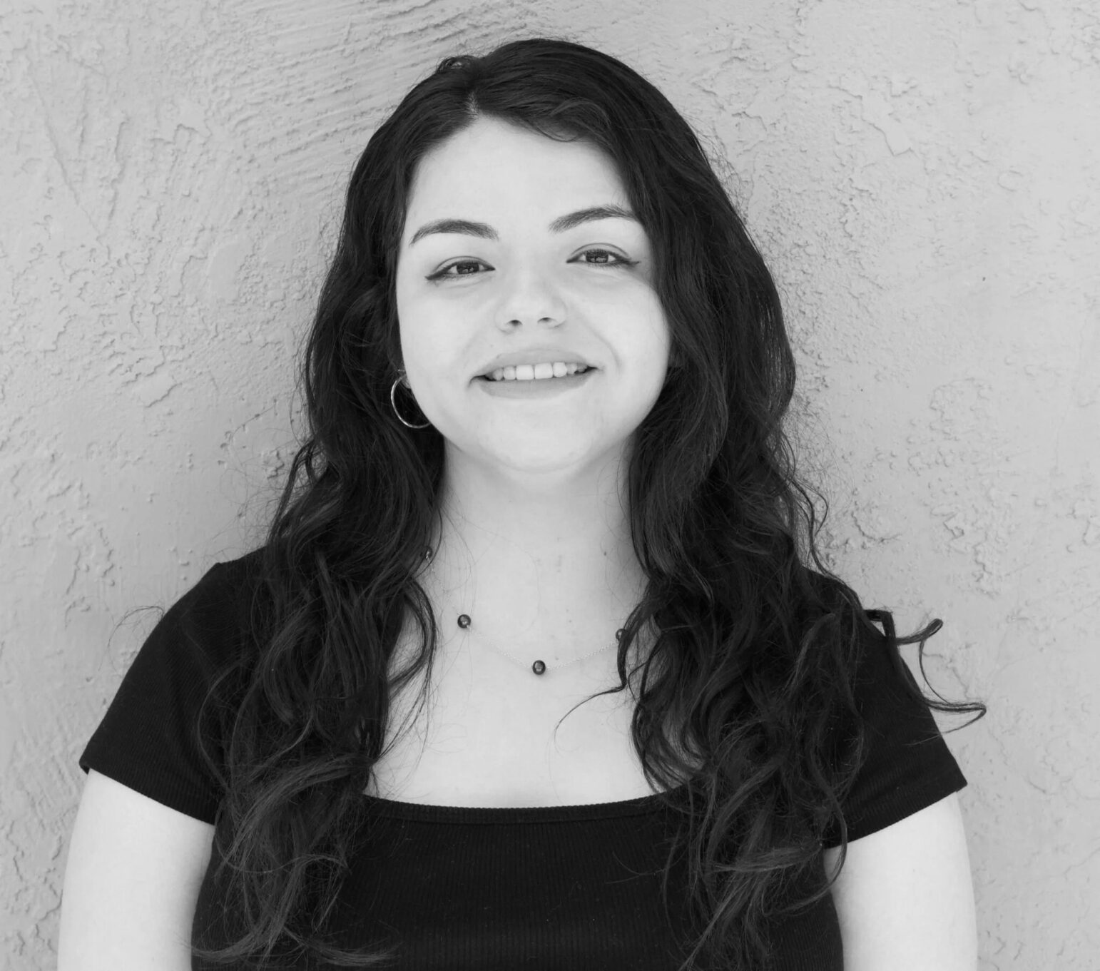 A professional black and white portrait of a smiling woman with dark hair and a dark top against a neutral background.