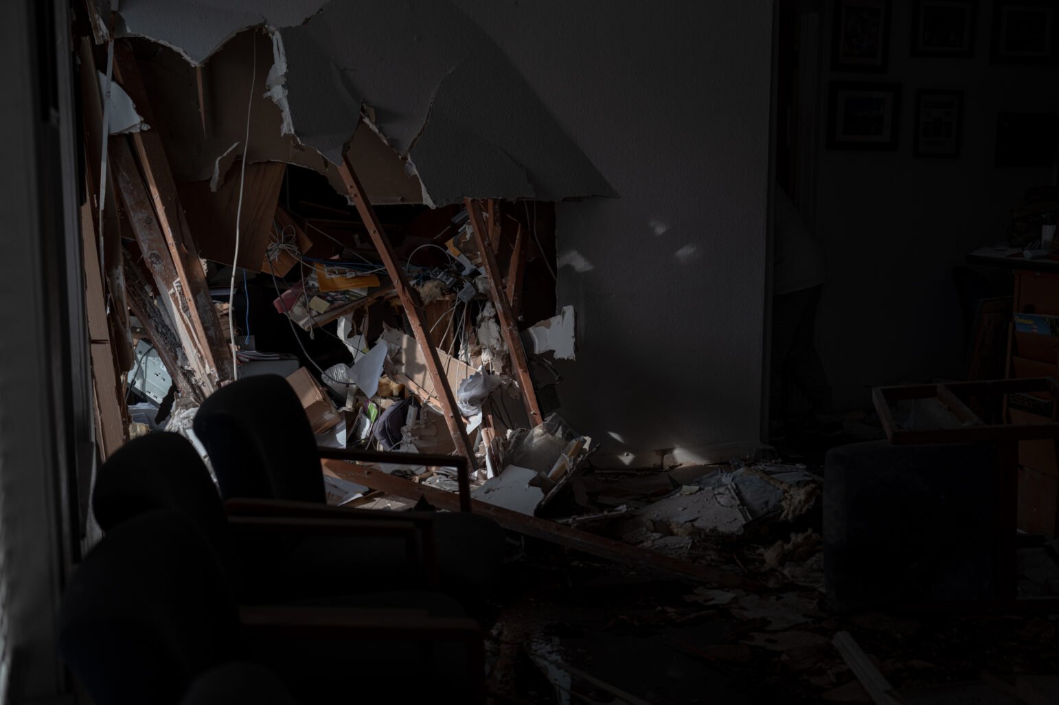 The interior of the Petrie Center building is shown, with significant damage to the walls, furniture, and belongings. Rubble and broken beams are scattered across the floor.