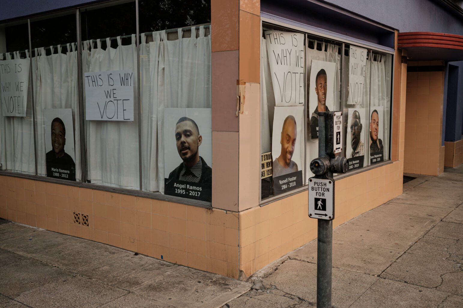 A storefront display features handwritten signs reading "THIS IS WHY WE VOTE" alongside large portraits of individuals with their names and birth-death years: Mario Romero, Angel Ramos, Ronell Foster, Eric Reason, Willie McCoy, and Sean Monterrosa. The display advocates for voting as a response to social justice issues.