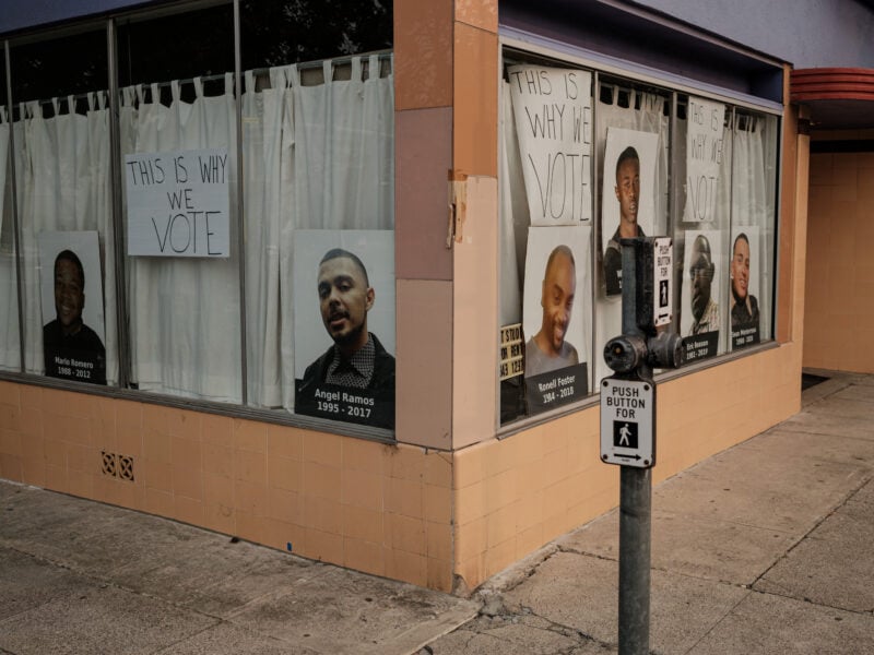 A storefront display features handwritten signs reading "THIS IS WHY WE VOTE" alongside large portraits of individuals with their names and birth-death years: Mario Romero, Angel Ramos, Ronell Foster, Eric Reason, Willie McCoy, and Sean Monterrosa. The display advocates for voting as a response to social justice issues.