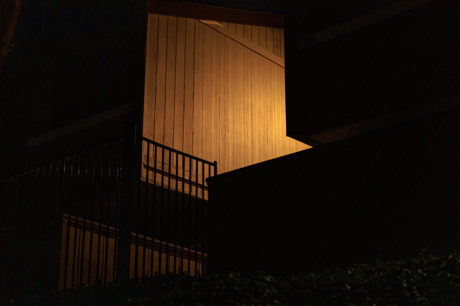 A staircase and balcony in warm yellow light contrasting the surrounding darkness at an apartment complex.