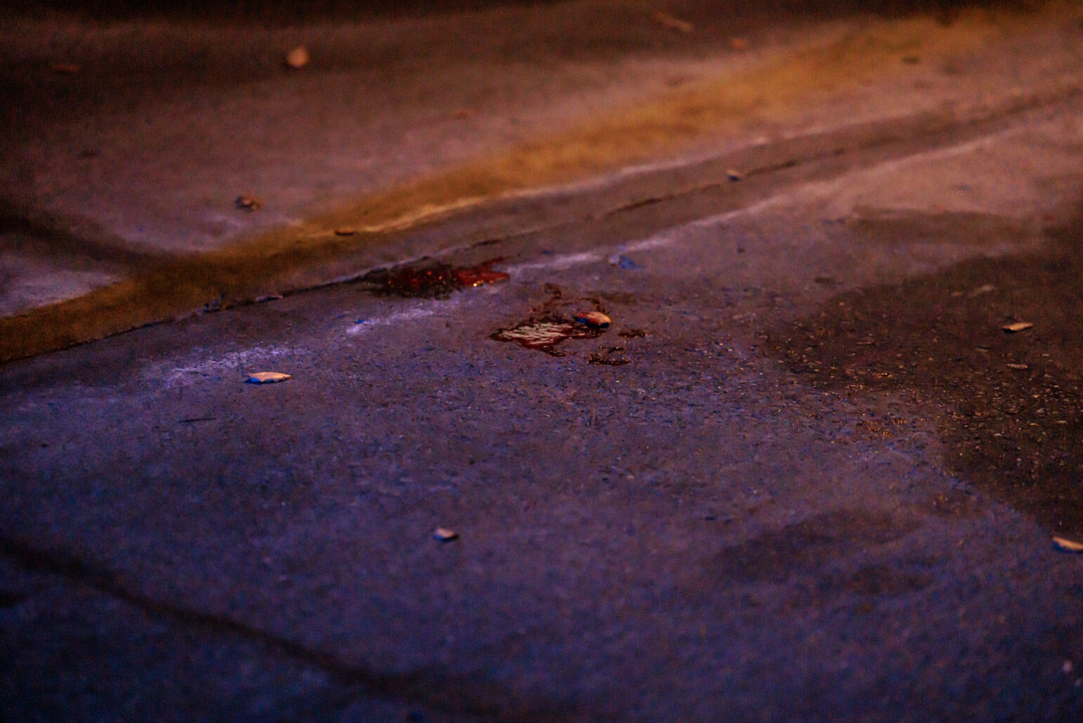 A close-up view of a bloodstain on a concrete surface, illuminated by ambient lighting, possibly at a crime scene.