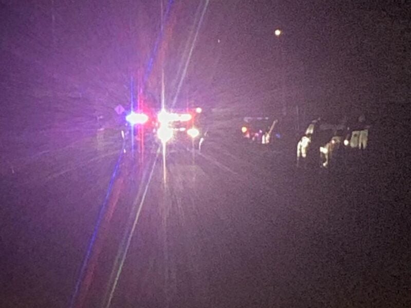 A night scene on a dark roadway where multiple emergency vehicles display flashing red and blue lights, creating pronounced lens flares that obscure much of the surrounding area.