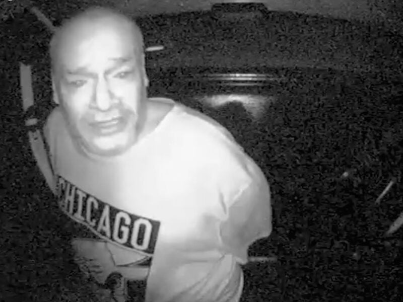 Grainy black-and-white surveillance image shows Darryl Mefferd, handcuffed and wearing a Chicago Bulls shirt, leaning forward in the backseat of a police vehicle. He appears distressed. A timestamp in the upper-left corner reads “2016-12-07 23:54:12.”