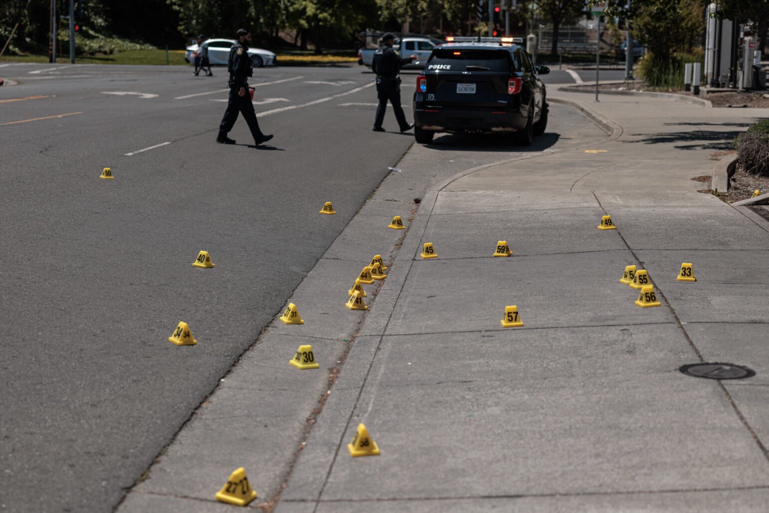 Dozens of numbered yellow prove a Vallejo crossing, while two police officers guard a patrol -SUV that blocks the shooting scene.