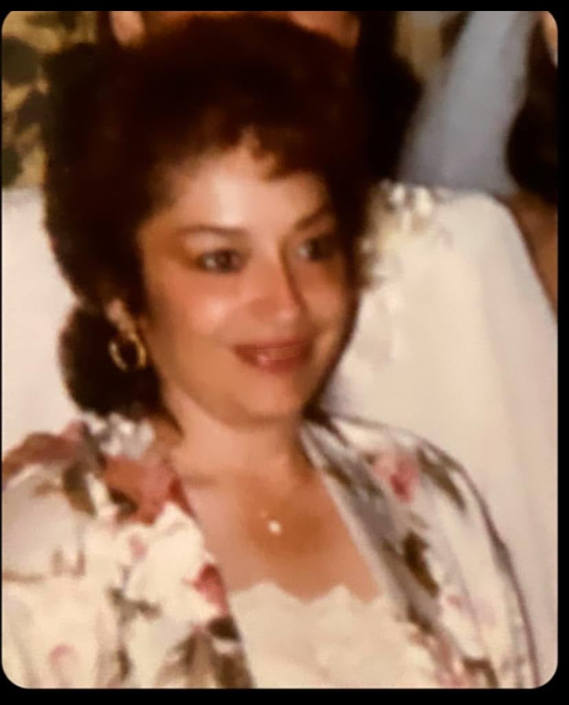 A candid color photo of Evangelina R. Humphrey in her middle age, smiling while wearing a floral-patterned blouse and earrings, with other people partially visible in the background.