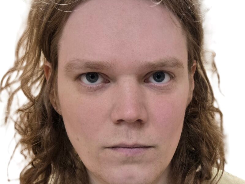 A booking photo shows a person with shoulder-length wavy hair wearing a beige shirt, looking directly at the camera with a neutral expression. The background is plain and white.