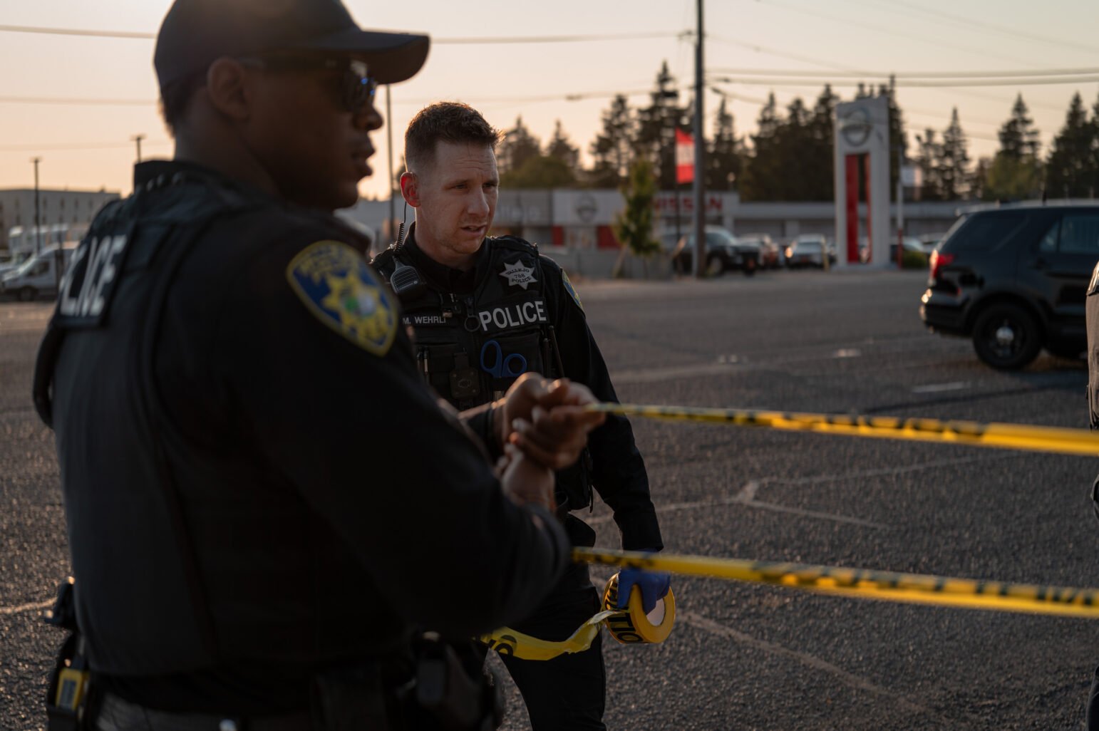 Vallejo police officers unroll yellow crime scene tape as the sun sets behind them.