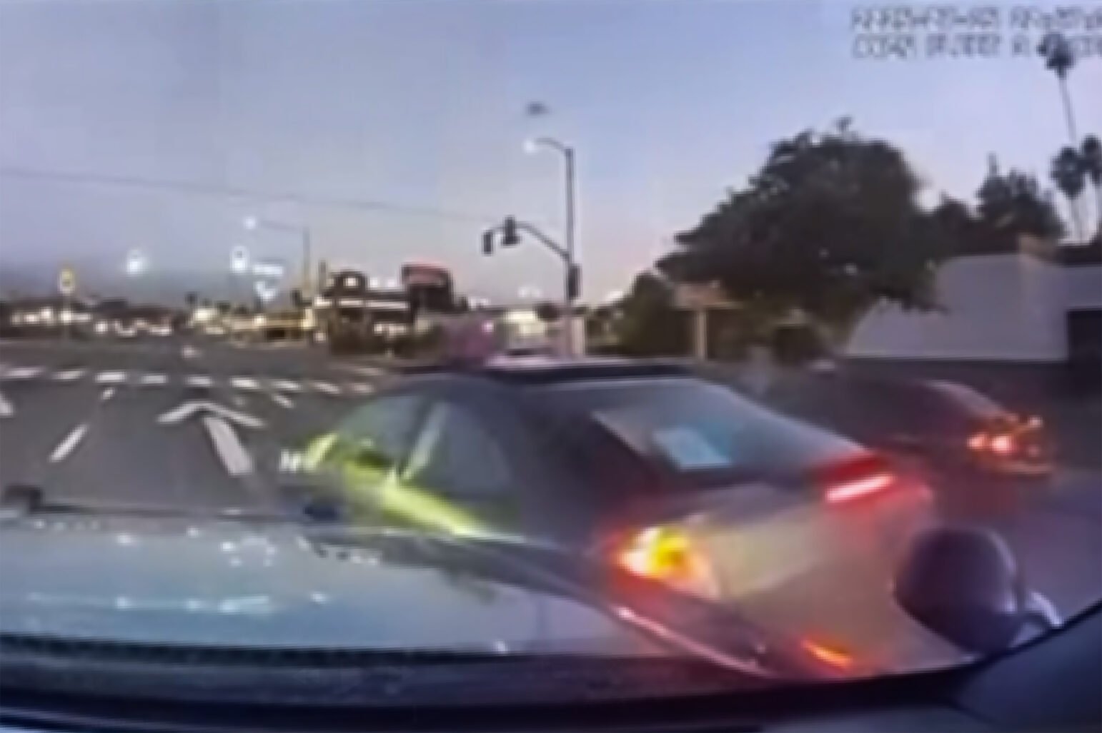 A dashcam view at dusk captures a police car ramming a black Mercedes at an intersection, causing the sedan to spin out of control.