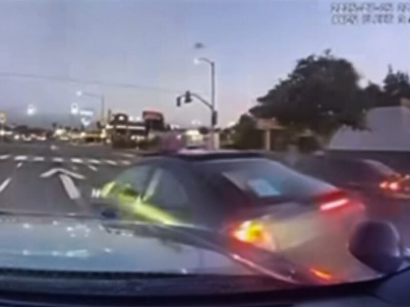 A dashcam view at dusk captures a police car ramming a black Mercedes at an intersection, causing the sedan to spin out of control.