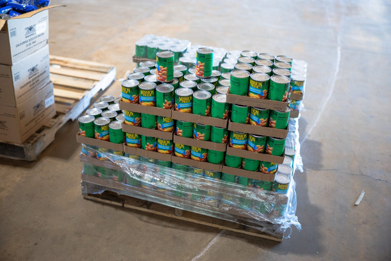 Shrink-wrapped pallet stacked with green-label canned fruit at a food distribution site.